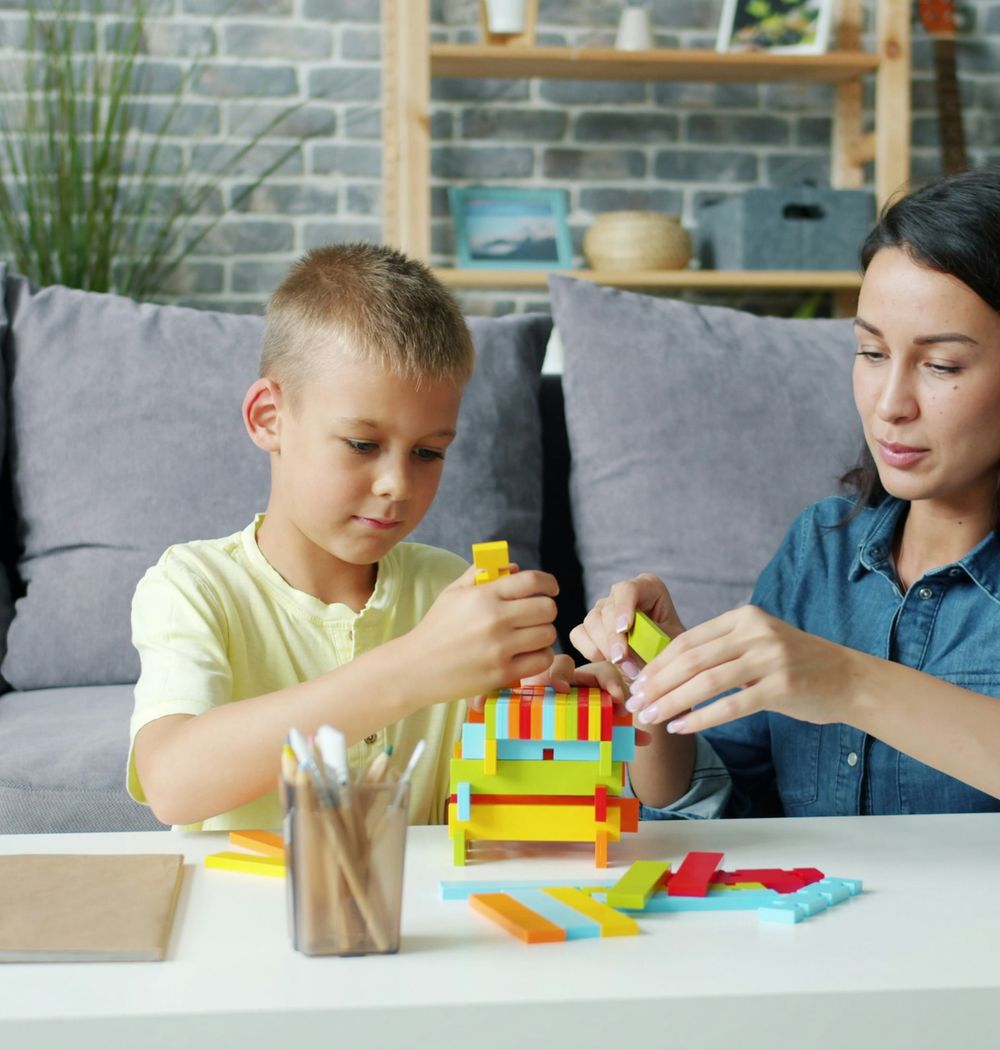 A woman and a young boy building with colorful blocks at home